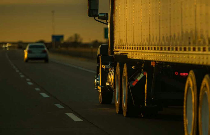 2289923583 Truck and car driving on highway at sunset.