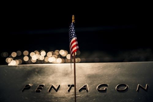 shutterstock_2321355077.jpg Close-up of a small American flag on a reflective surface with the word PENTAGON in the background