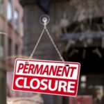 A sign reading 'PERMANENT CLOSURE' hanging in a shop window