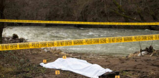 Crime scene near a river with covered body.