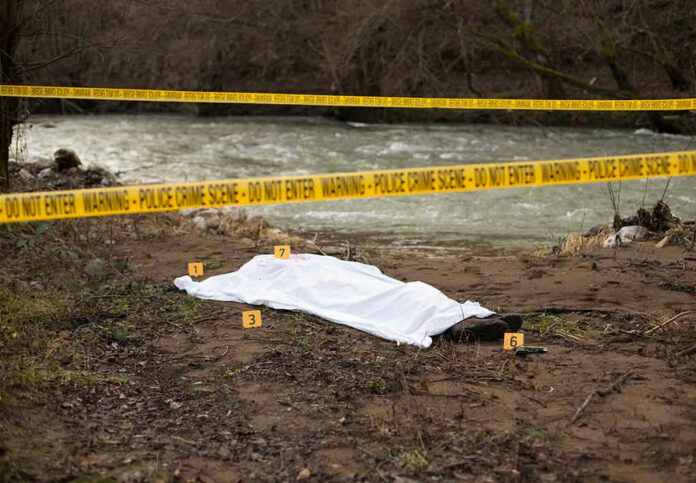 792627442 Crime scene near a river with covered body.