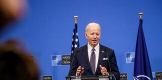 man in suit speaking at a podium with NATO backdrop