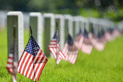 shutterstock_1041465589.jpg American flags beside gravestones in a cemetery.