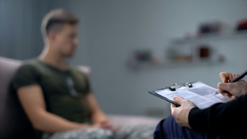 shutterstock_1486344695 Therapist taking notes while talking with a young man.