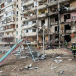 Russia’s RETALIATION Strikes Fear in Kyiv Damaged apartment building with debris scattered firefighters present.