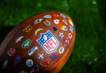 NFL Star’s Shocking ARREST – What’s the Truth? Close-up of an NFL football featuring various team logos on its surface