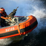 FISHERMEN SLAUGHTERED — Pentagon Hides the Bodies… Person on orange boat holding machine gun.