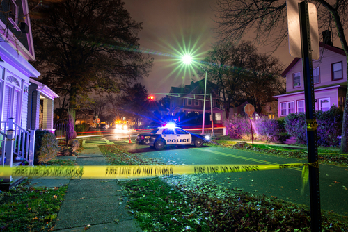 Crime,Scene,With,Tape,And,Police,Car Police car with flashing lights at a crime scene surrounded by caution tape