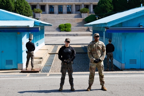 Two military personnel standing in front of blue buildings at a border