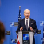 man in suit speaking at a podium with NATO backdrop