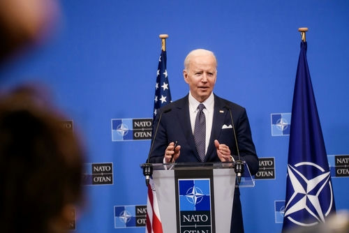 man in suit speaking at a podium with NATO backdrop