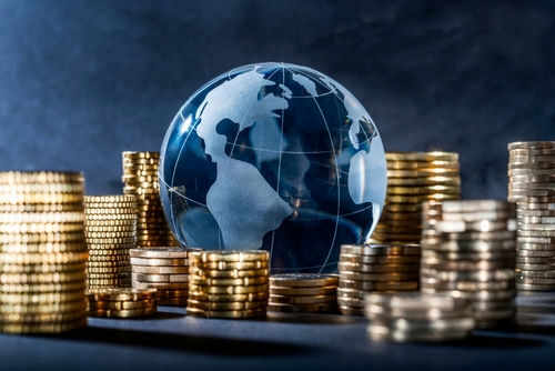 shutterstock_2154195865 Glass globe surrounded by stacks of gold coins.