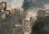 A cityscape showing damaged buildings and thick smoke rising from the ground