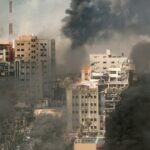 Nightmare: Hundreds of Drones, Dozens of Missiles A cityscape showing damaged buildings and thick smoke rising from the ground