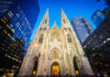 Gothic cathedral illuminated at dusk surrounded by modern skyscrapers