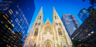 Gothic cathedral illuminated at dusk surrounded by modern skyscrapers
