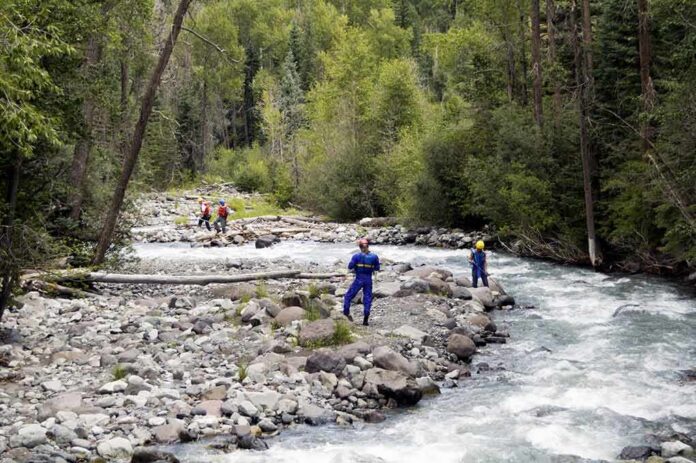 shutterstock_829761 Rescue workers in helmets standing along a fast-flowing forest river