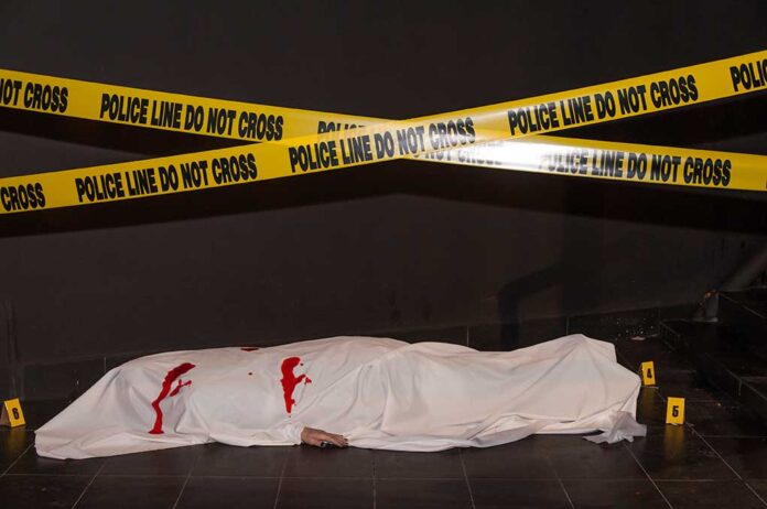 Body under white sheet with police line tape.