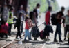 Group of people with luggage walking on train tracks.