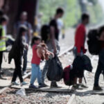 Group of people with luggage walking on train tracks.