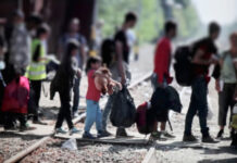 Group of people with luggage walking on train tracks.