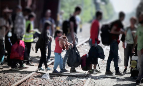 Group of people with luggage walking on train tracks.