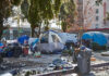 Homeless encampment with tents and trash in urban area.