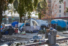 Homeless encampment with tents and trash in urban area.