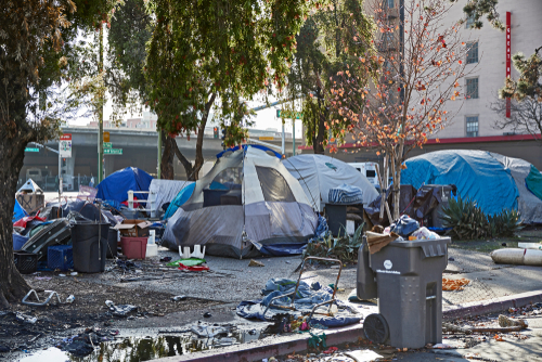 Homeless encampment with tents and trash in urban area.