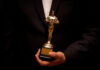 Person holding an Oscar statuette in formal attire.