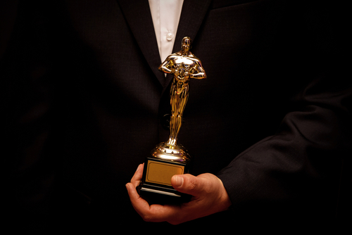 Person holding an Oscar statuette in formal attire.