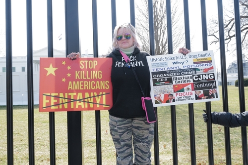 Protester holding fentanyl awareness signs outside White House fence.